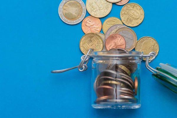 Coins in a glass jar, scattered change currency money on a blue background. a place for text. Concept: financial crisis, decrease in income, capital investments.