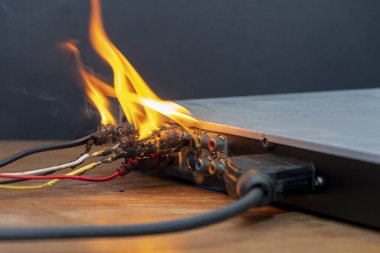 A DVD player is burning on the table, network cables are burning and sparking, flames are rising up, a fire has started in the apartment.