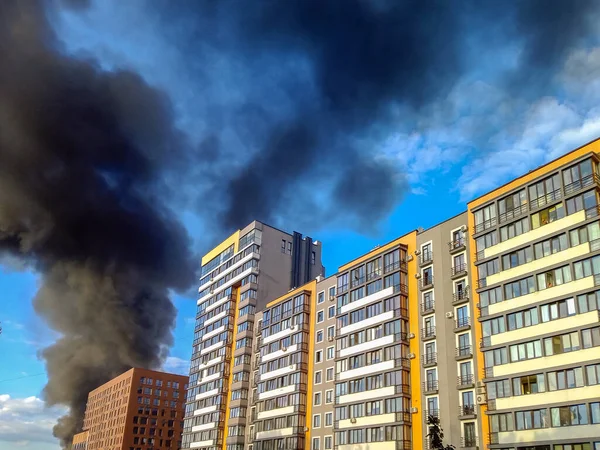 Burning building of newly built high-rise buildings.Black smoke rises up against the blue sky and clouds.