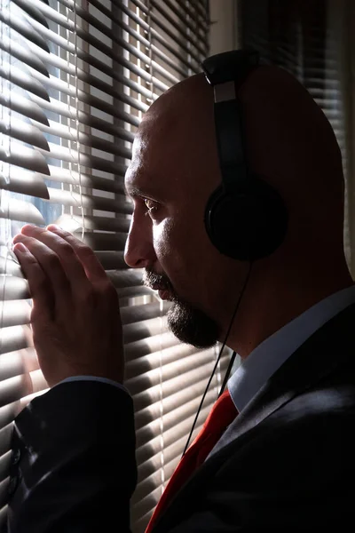 ヘッドフォンを持つ男は 窓のブラインドを通って見えます 会話に盗聴 人々のスパイ コンセプト ミッション上の特別なエージェント 監視と盗聴 — ストック写真