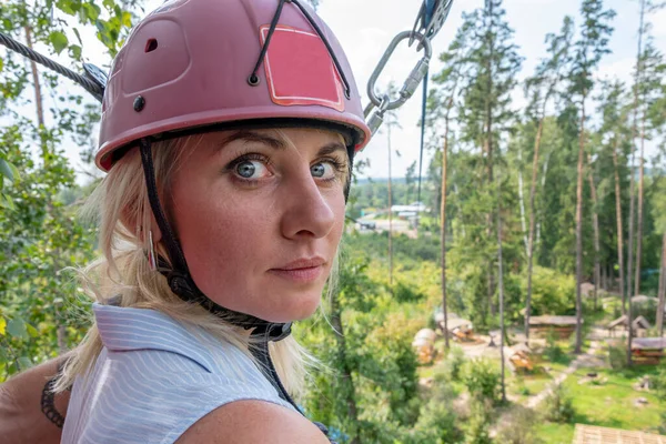 portrait of a frightened blonde woman in a helmet, preparing to jump from a height on a rope.