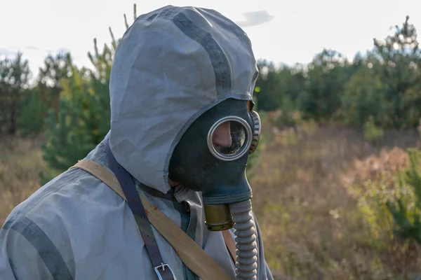 A military man in chemical protection and a gas mask measures the radiation level with a dosimeter in nature, smoke from a fire. Concept: radiation leakage, radioactive hazard
