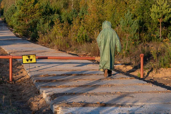 A Russian military man in chemical protection enters the zone of radioactive contamination, a sign of radiation danger against the background of a forest and a road.