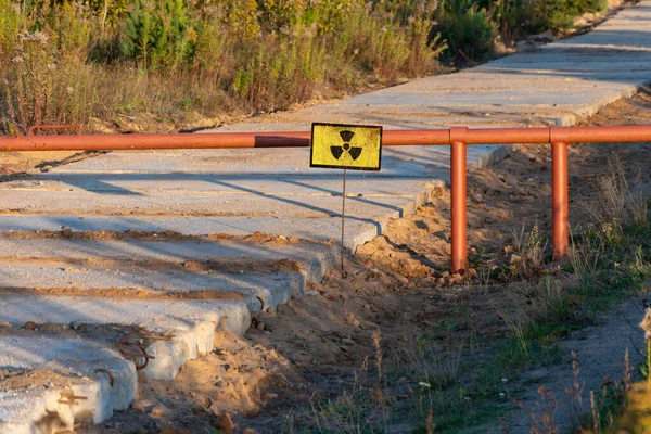 A sign of radioactive danger on the barrier against the background of a forest yellowed by radiation. Concept: radioactive hazard, impact on nature, danger zone.