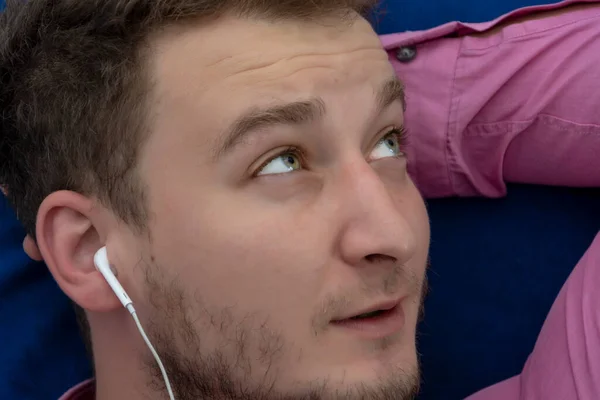一名身穿衬衫的35 38岁男子躺在一张蓝色的床上 用有线耳机听音乐 梦幻般的心情 在沙发上放松 — 图库照片