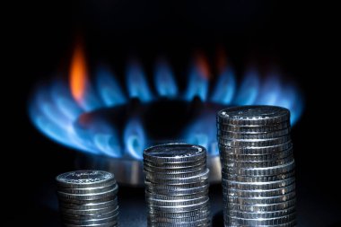 Yanan bir gaz ocağının arka planında metal para yığını, karanlık tonlar, metin için bir yer, kopyalama alanı. Kavram: artan benzin ve enerji fiyatları, artan kira.