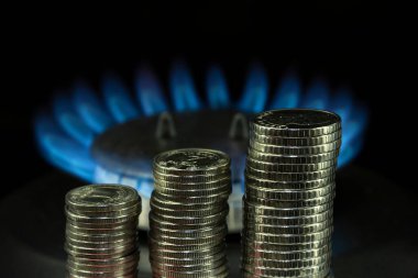 Yanan bir gaz ocağının arka planında bir yığın Ukrayna Hryvnia sikkesi, karanlık ton. Kavram: Ukrayna 'da artan gaz ve enerji fiyatları.