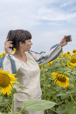 Koyu renk saçlı güzel bir Ukraynalı kadın 35-40 yaşlarında ayçiçeklerinin arasında bir tarlada selfie çekiyor..