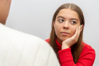 Hafif bir arka planda genç bir kız, sıkılmış bir bakışla erkeğini dinler, başını elinin üzerine koyar. Kavram: ilginç olmayan konuşma, sıkıcı konuşma.