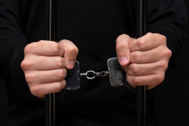 Kelepçeli bir mahkum parmaklıkları sıkıyor, koyu renk, seçici odaklanma, ön görüş..