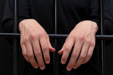 Hüküm giymiş adam ellerini mahkeme salonundaki parmaklıklara asmış. Karanlık bir tonda, seçici bir odak noktasında..