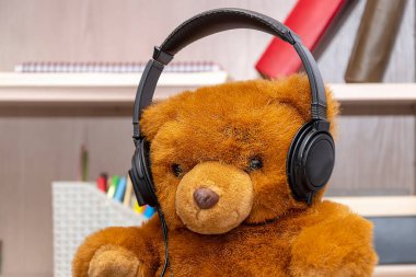 Tarafsız bir arka planda kulaklığı olan oyuncak ayı. Kavram: Müzik dinlemek.