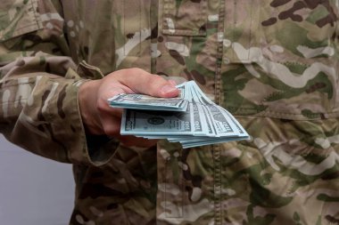 A soldier holds out a wad of $100 paper bills, close-up, selective focus. Concept: Army pay, contract service, performance bonus, bribery of soldiers and officials. clipart