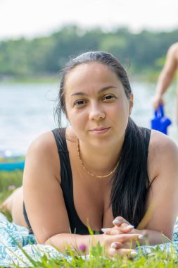 35-40 yaşlarında güzel bir esmer gölün ve doğanın arka planında kumsalda bronzlaşıyor..