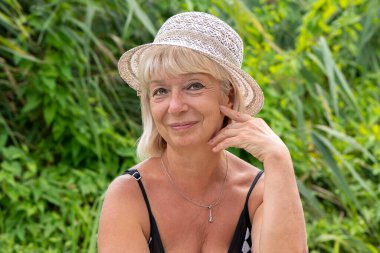 Doğanın arka planında hasır şapkalı 60-65 yaşlarında yaşlı bir kadının portresi..