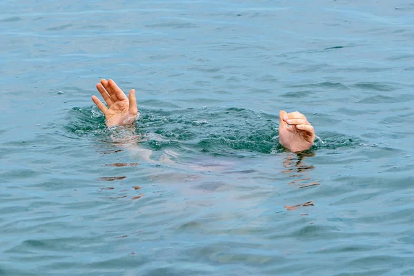A man is drowning in the water. Two hands stick out of the water against the background of the waves. Concept: drowned people, rescue of a drowning person, danger of drowning.