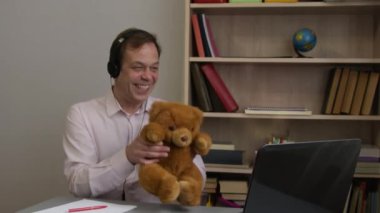 Oyuncak ayıyı elinde tutan bir adam çocuğuyla bilgisayarla iletişim kuruyor..