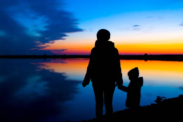 妈妈和孩子在湖边散步的轮廓，秋天的落日. — 图库照片