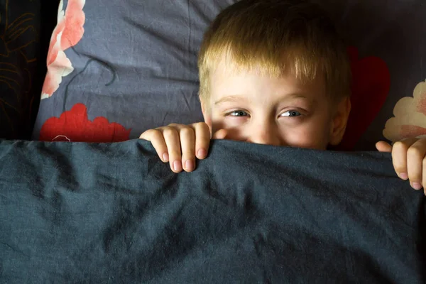 Um rapaz adulto espreita debaixo do cobertor. — Fotografia de Stock