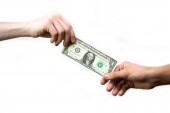 Ruka předává dolar do druhé ruky na bílém pozadí.