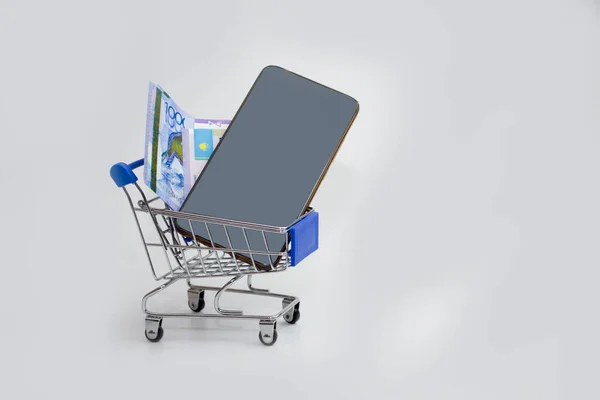 W wózku na białym tle jest telefon z rachunkiem tenge, zakup telefonu, lub płacenie za pośrednictwem aplikacji mobilnych. — Zdjęcie stockowe