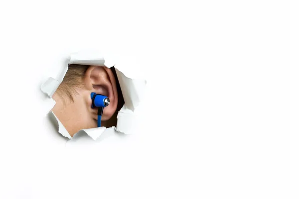 Fones de ouvido azuis no meu ouvido saem através de um buraco em um fundo branco. — Fotografia de Stock