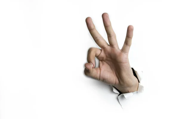 Fingers in the form of an OK gesture stick out of a hole on a white background. — Stock Photo, Image