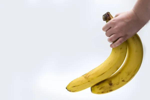 Het kind houdt bananen in zijn hand op een witte achtergrond. — Stockfoto
