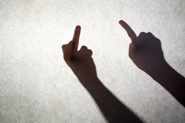 Shadow silhouette of a human hand on a wall. fuck sign. A rude gesture of the middle finger raised up denoting anger — Stock Fotó