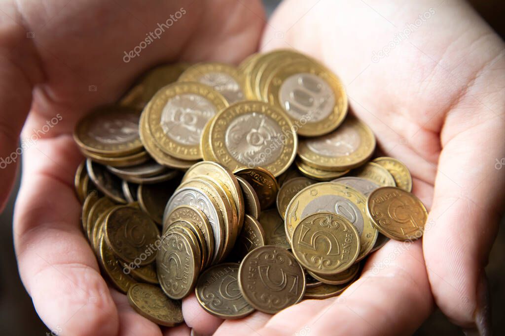 Womens hands hold a bunch of coins with a face value of 100 tenge, the subsistence minimum.