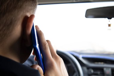 Genç bir adam araba kullanırken telefonla konuşuyor..