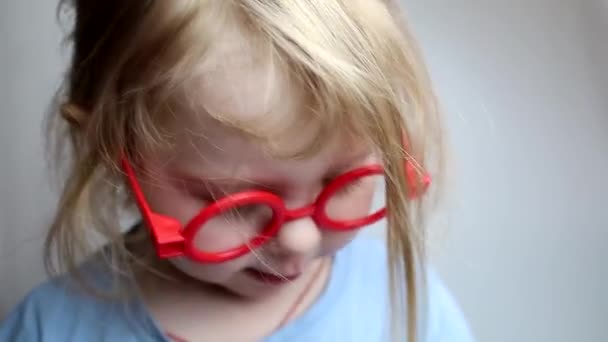 Una ragazza con i capelli ondulati in occhiali giocattolo rosso. — Video Stock