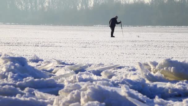 Зимний рыбак проверяет прочность и толщину льда, блики на поверхности льда. Зимний солнечный день. — стоковое видео
