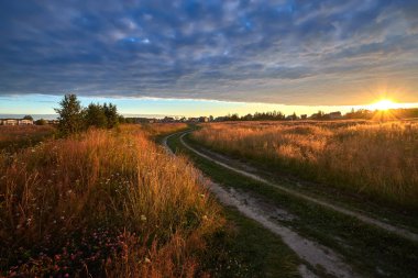 Gün doğumunda kırsal toprak yolu olan manzaralı bir yer. Yaz manzarası.