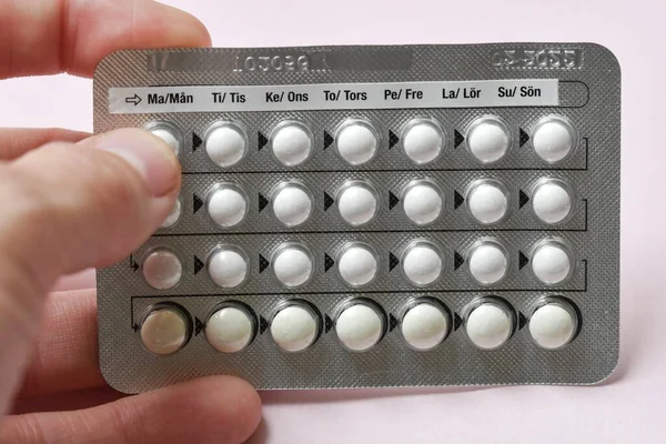 A woman holding a full chart of birth control pills on pink background