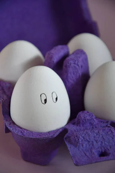 Photo of funny eggs with painted faces in a purple carton, preparation for Easter