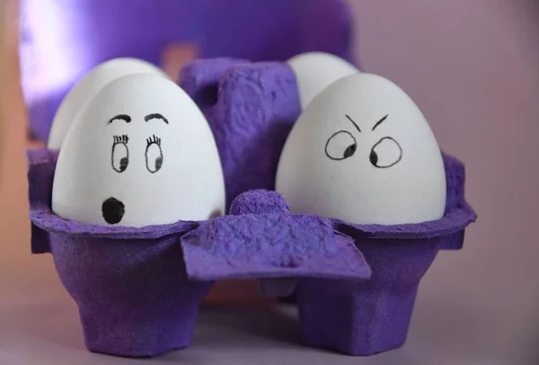 Photo of funny eggs with painted faces in a purple carton, preparation for Easter