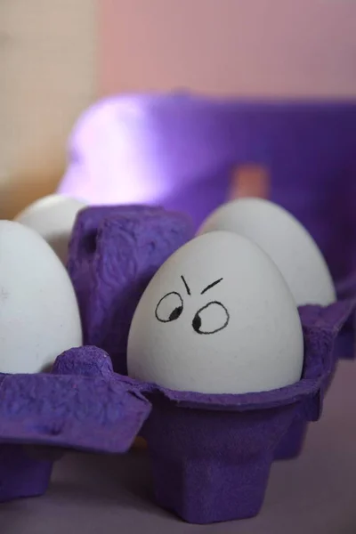 Photo of funny eggs with painted faces in a purple carton, preparation for Easter