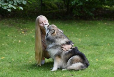 Bir kadının portresi ve arka bahçede birbirine sarılan Fin Lapphund köpeği.