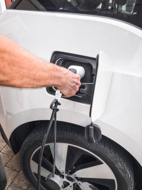 Şarj aletini beyaz elektrikli arabasına takan bir adam.