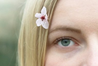 Sarışın bir kadının saçlarında küçük bir kiraz çiçeğinin yakın çekimi ya da makrosu.