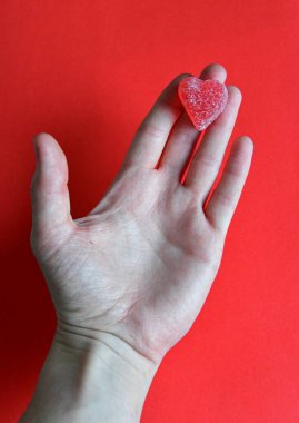 Kırmızı arkaplandaki kadının elinde kırmızı jöleli şeker kalbi fotoğrafı.