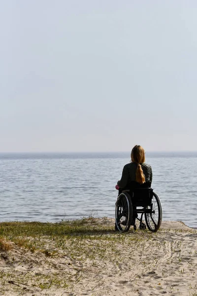 Silhouette of a person in wheelchair sitting and watching the sea from the beach