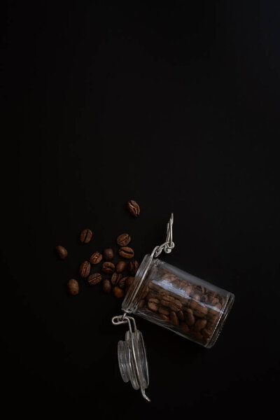 Studio photo of brown coffee beans in a glass jar on black background