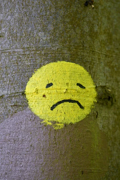 A sad yellow smiley face painted on a tree in nature