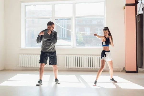 Un allenatore esperto mette la tecnica dei colpi ad una giovane ragazza nella sala da boxe — Foto Stock
