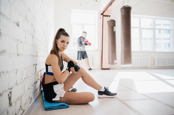 흰 벽돌 벽에 기대어 권투를 하고 있는 한 소녀가 자신의 손에 권투를 하기 위해 스포츠용 붕대를 감고 있다 — 스톡 사진