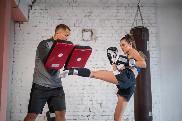 Femmina combattente arti marziali praticando calcio gamba o calcio alto con il suo allenatore in uno studio di boxe nella giornata di sole. — Foto Stock