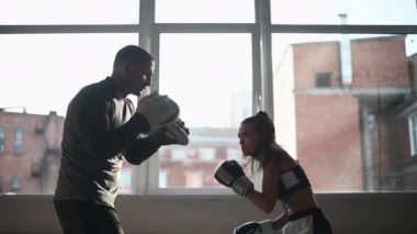Genç bir kız kickboks antrenmanı yapıyor ve profesyonel bir boksörle pençe vuruşu yapıyor.