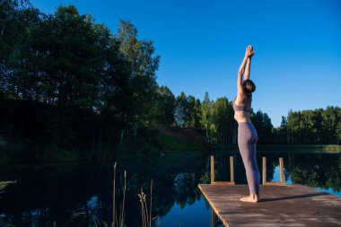 Gün doğumunda gökyüzüne karşı yoga yapan genç bir kadın. Oldukça zayıf bir kadın egzersiz yapıyor. Sağlık, meditasyon, sağlık, farkındalık konsepti.